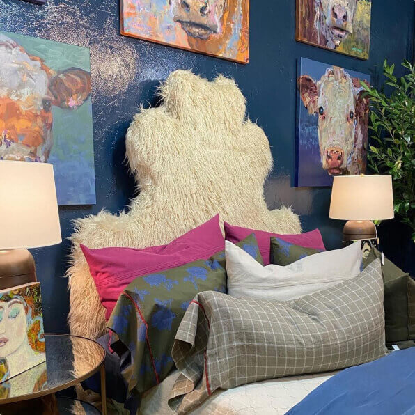a bed with colorful pillows next to a wall with pictures of cows